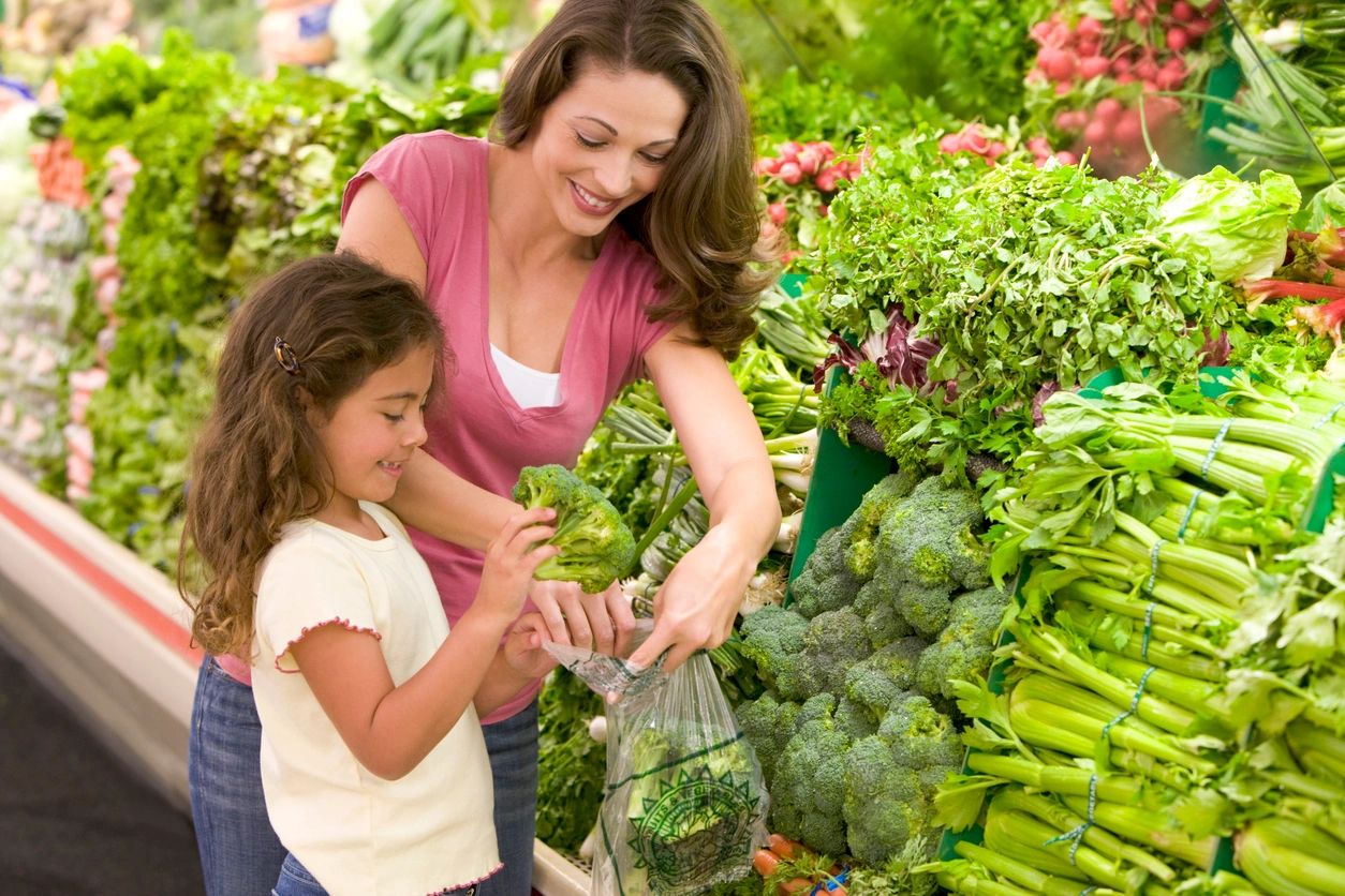 A woman and girl shopping for vegetables at the market.